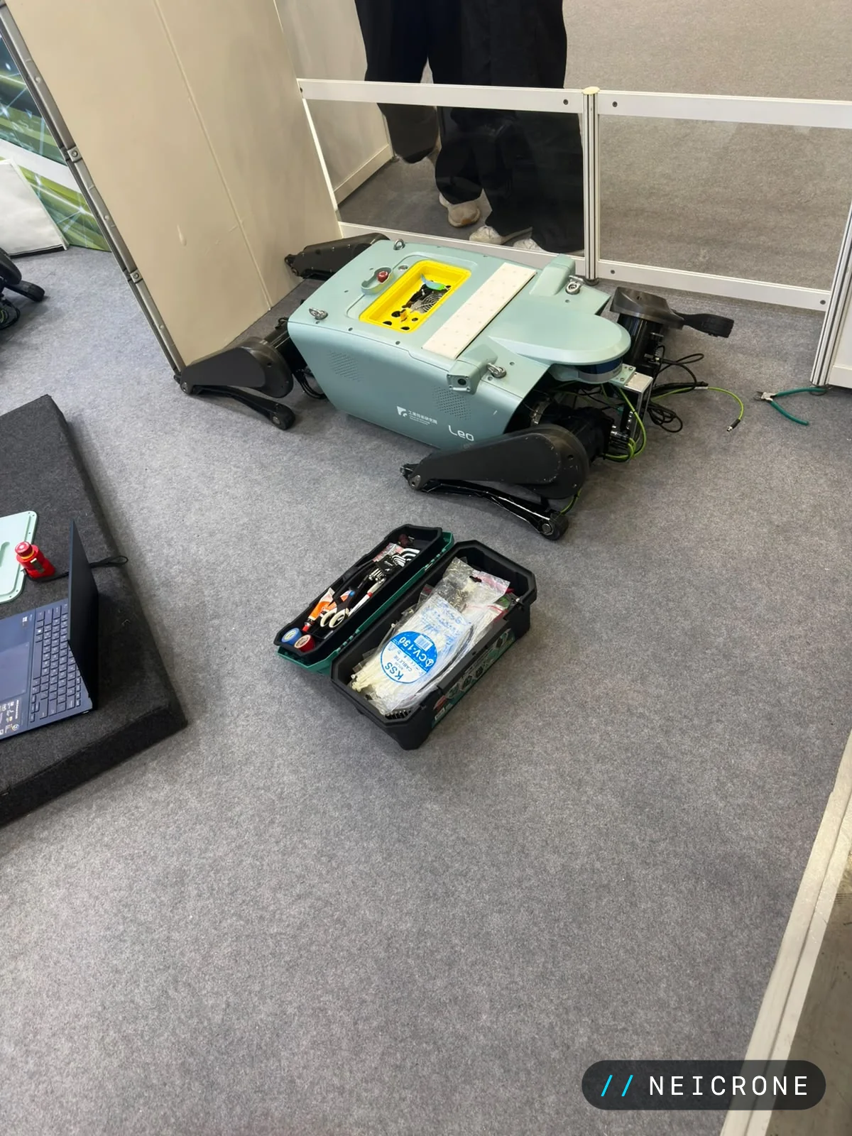 Quadruped robot lying open on the show floor beside a toolbox during maintenance