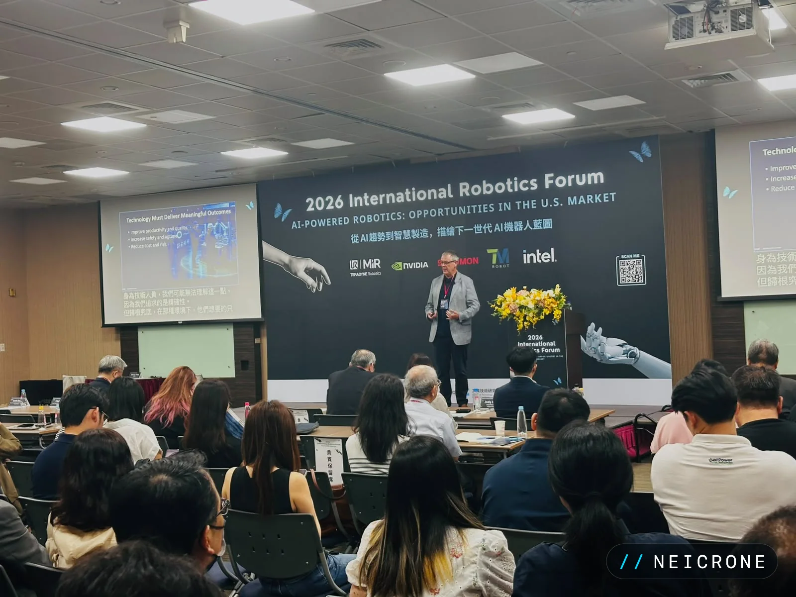 A speaker presenting on stage at the 2026 International Robotics Forum to a seated audience