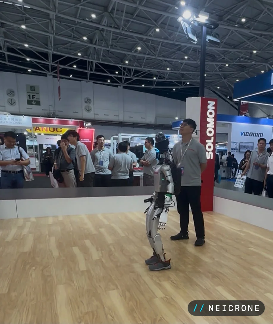 Humanoid robot walking across a demonstration floor with an engineer beside it